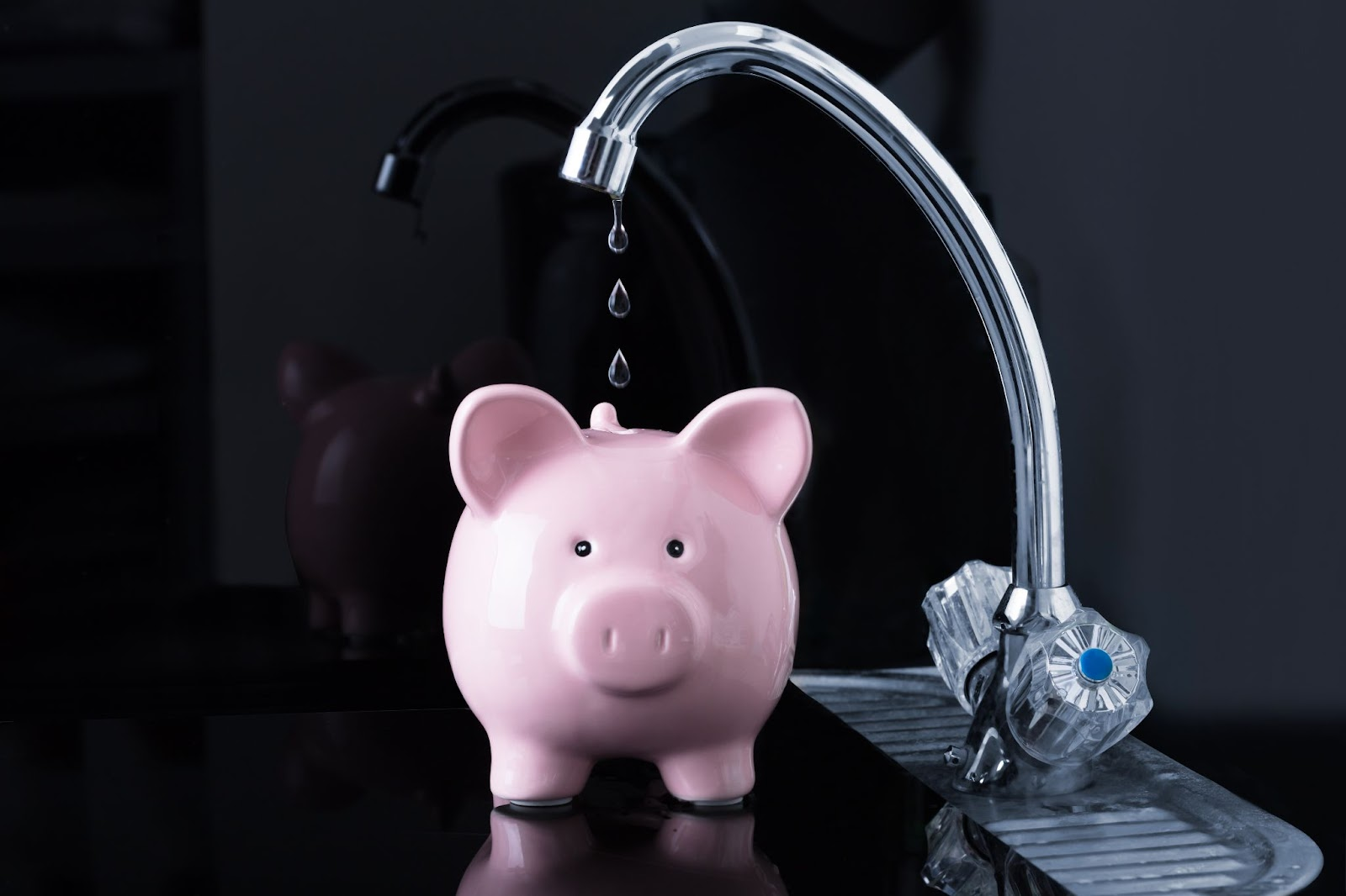 Leaky faucet dripping water into cute pink piggy bank