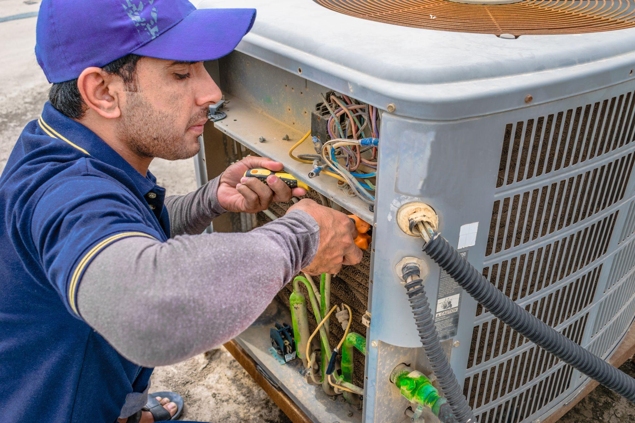 Technician repairs outside AC unit as wires and cables are visible