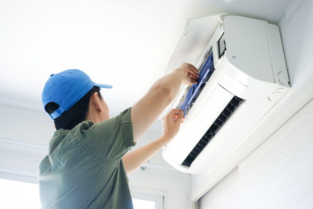 Technician servicing a ductless mini-split high up on a white wall.