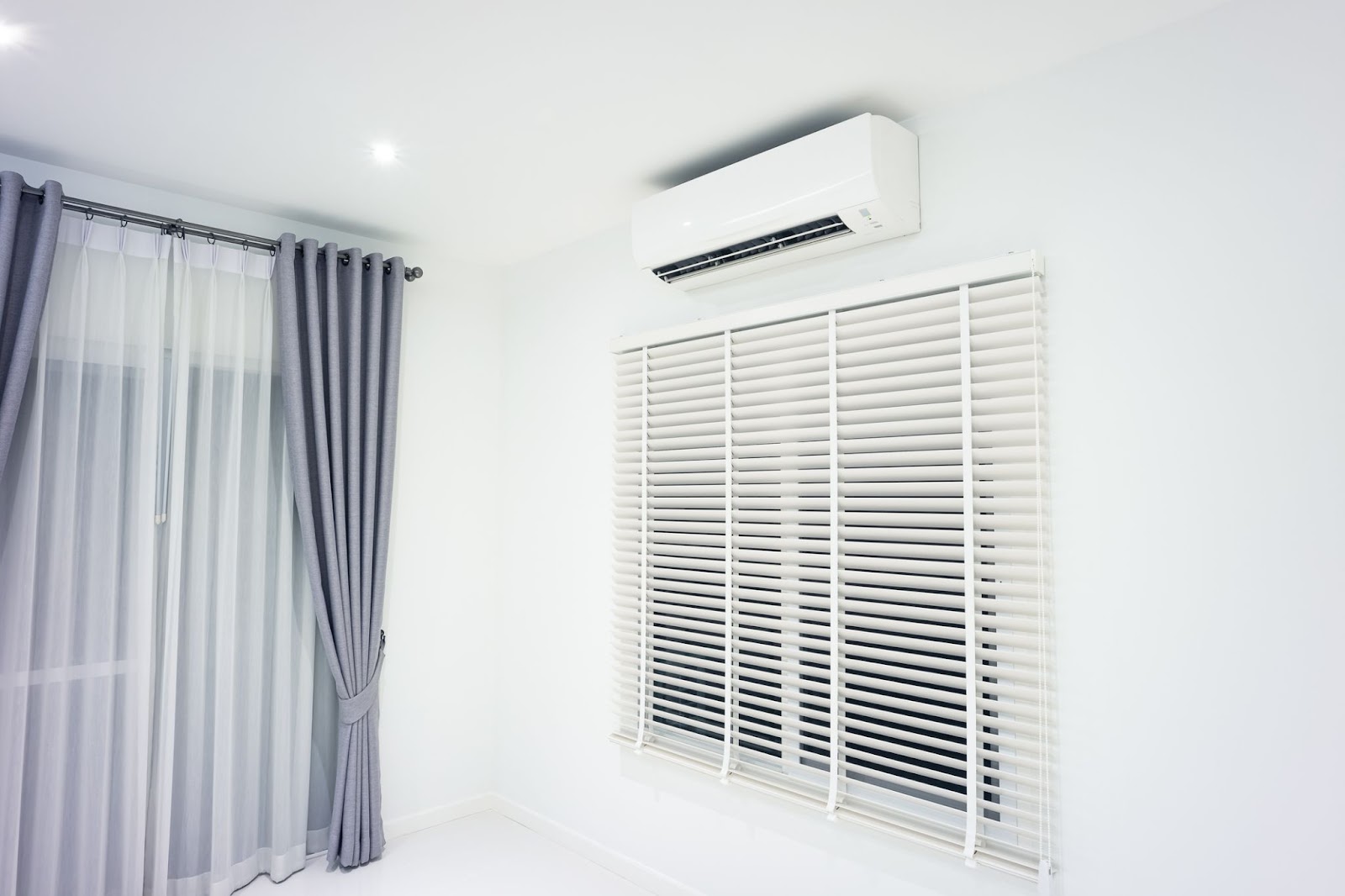 Ductless air conditioner on wall above curtained window in a white clean room