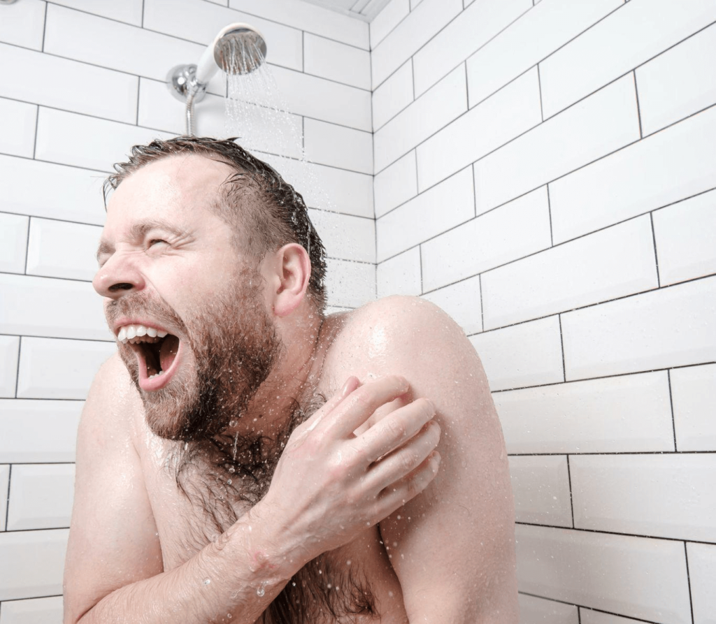 Man in shower shivering and screaming from cold water
