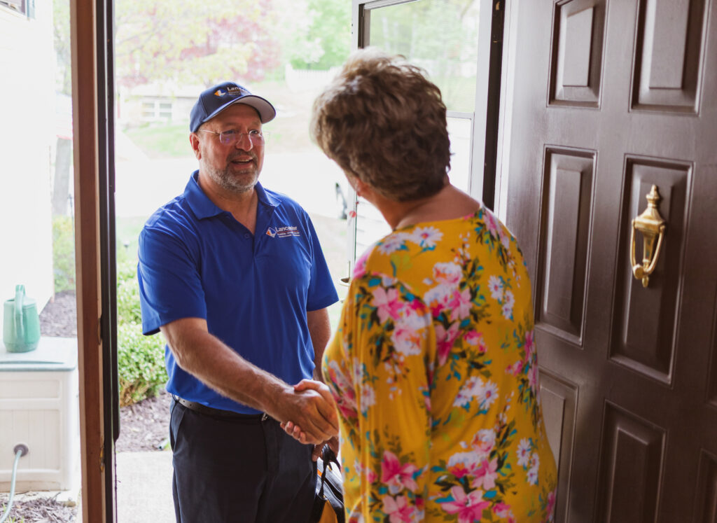 Lancaster Plumbing, Heating, Cooling & Electrical employee greets homeowner at front door, shaking hands.