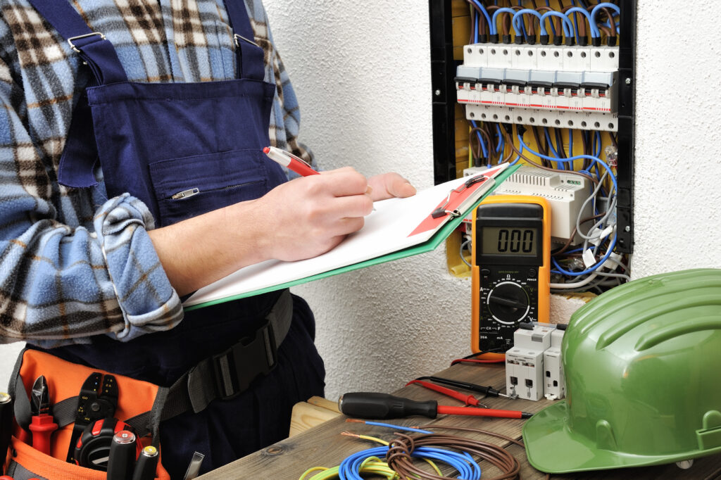 Electrician writes in a notebook the data collected on a residential electric panel